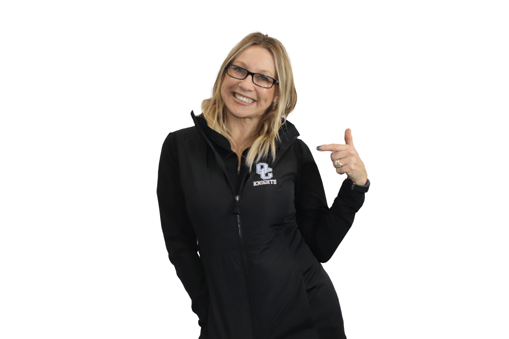 Blonde woman wearing a black OC Knights embordered vest and pointing to it.